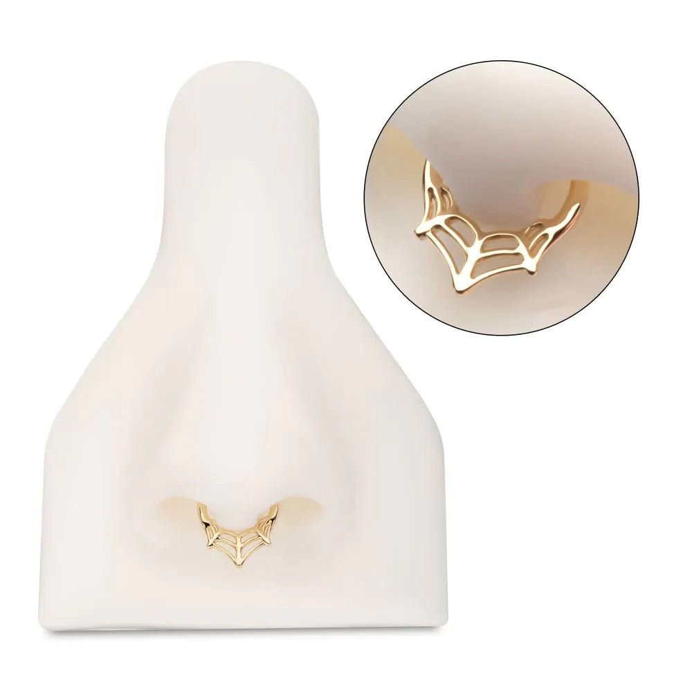 A gold spiderweb-shaped clicker ring, on display in the septum piercing of a model nose.