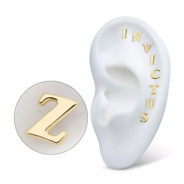 A collection of gold stud earrings shaped like the letters I N V I C T U S, on display in a model ear with a separate close-up shot of the Z.