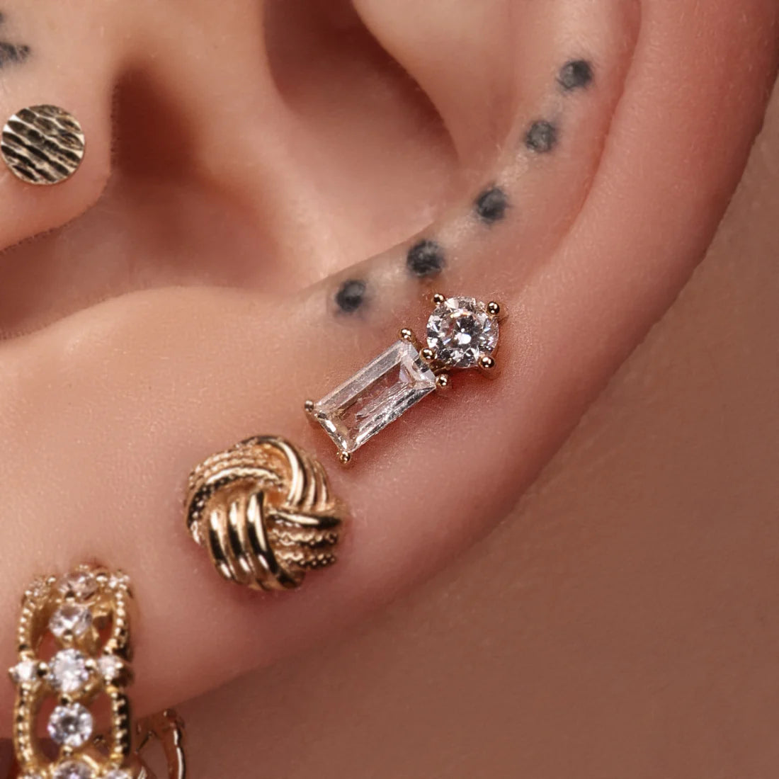 A close-up of an ear with several earrings and tattoos.